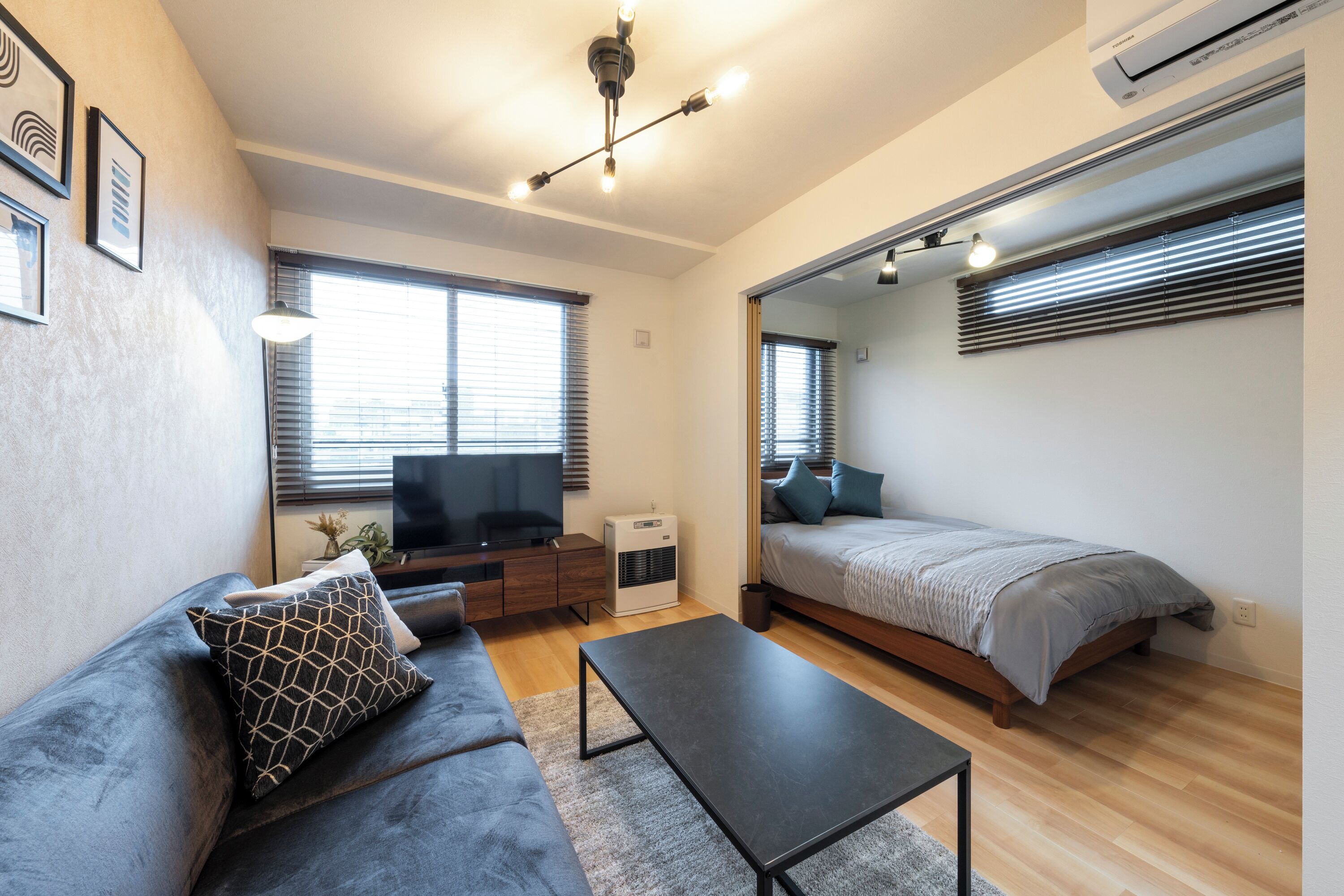 A modern living room with a sofa, a coffee table, a TV, and a bed.
