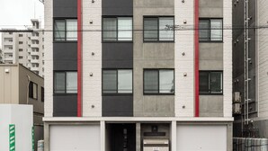 A multi-story building with a garage entrance, large windows, and a red stripe on the facade. - UNISON (Sapporo)