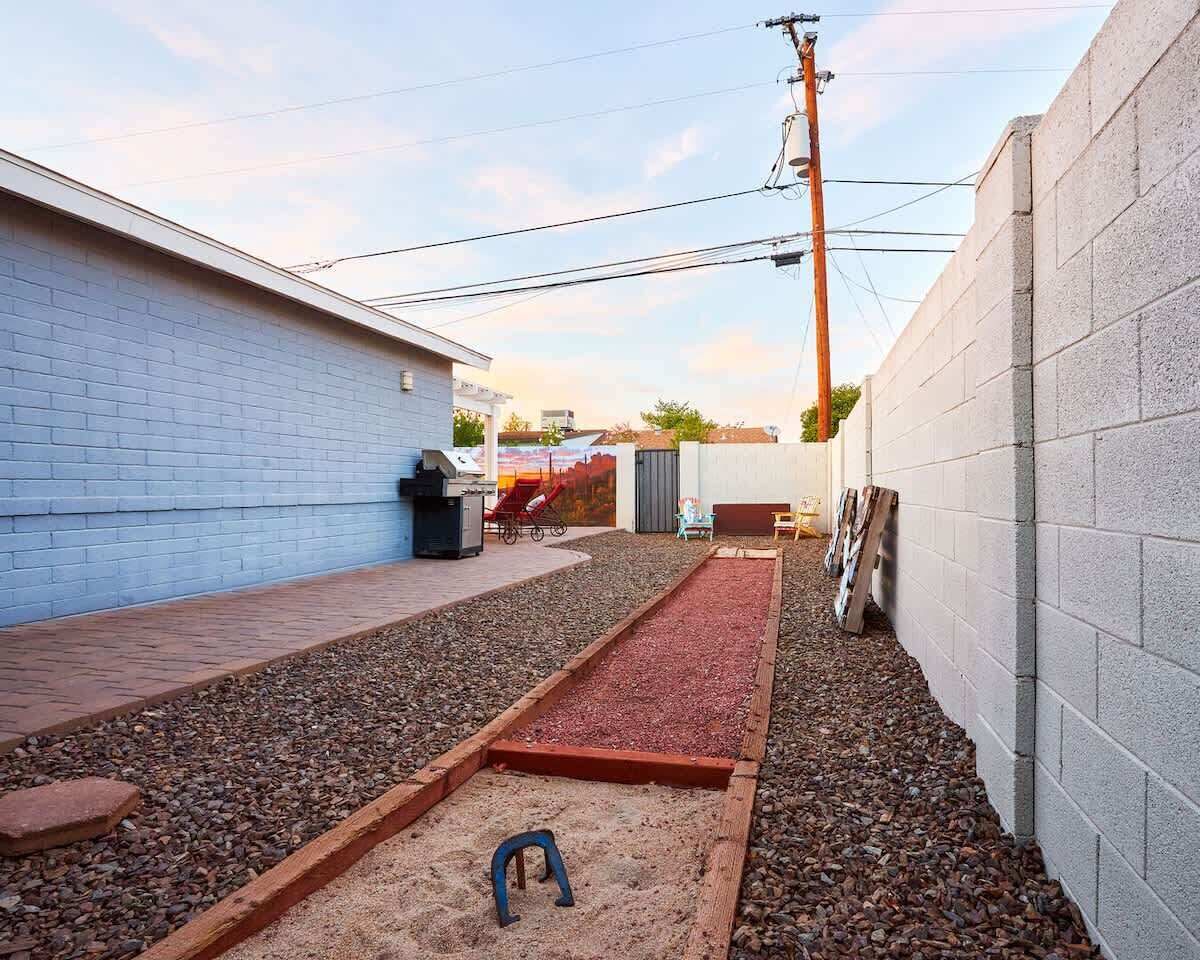 Un patio trasero con un sendero de grava, un arenero y una parrilla para barbacoa.
