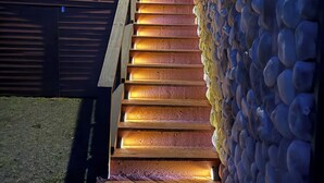 Una escalera de madera que conduce a una casa moderna, con un muro de piedra a un lado.