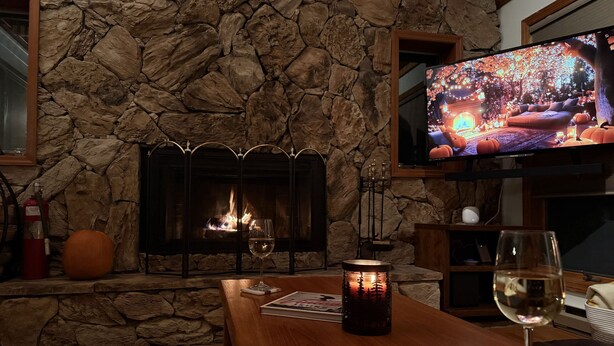 Una chimenea de piedra con un televisor encima, una mesa de madera con una vela y una copa de vino.