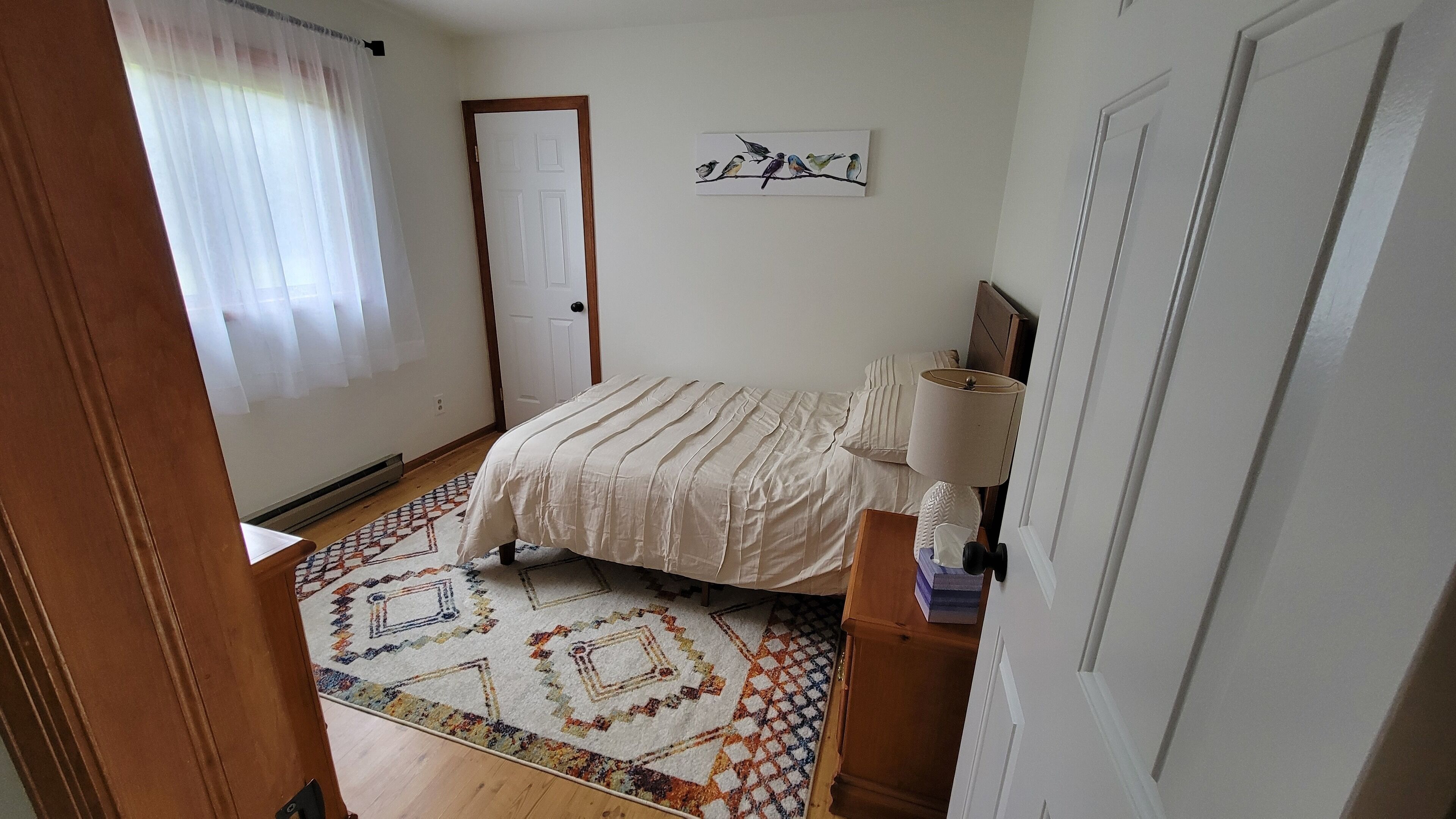 A bedroom with a bed, a bedside lamp, a patterned rug, and a wall-mounted artwork.