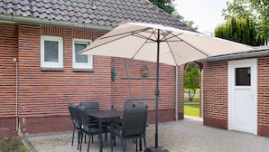 Un patio con una mesa y sillas, un paraguas grande y un edificio de ladrillo con una puerta y ventanas.