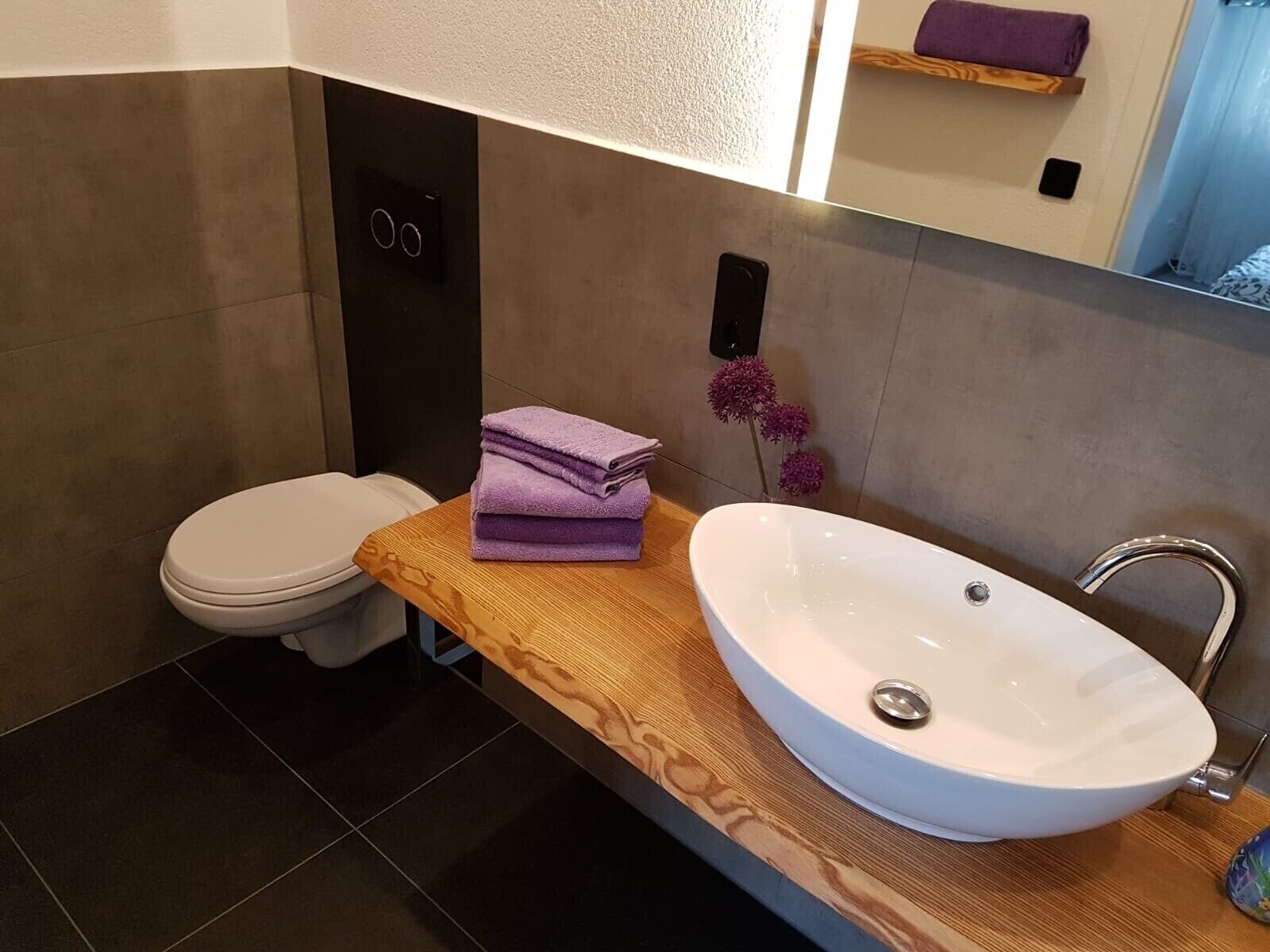 A modern bathroom with a wooden vanity, a white sink, and a toilet.