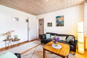 Ett vardagsrum med ett träpanelat tak, en svart lädersoffa, ett träbord och en golvlampa.