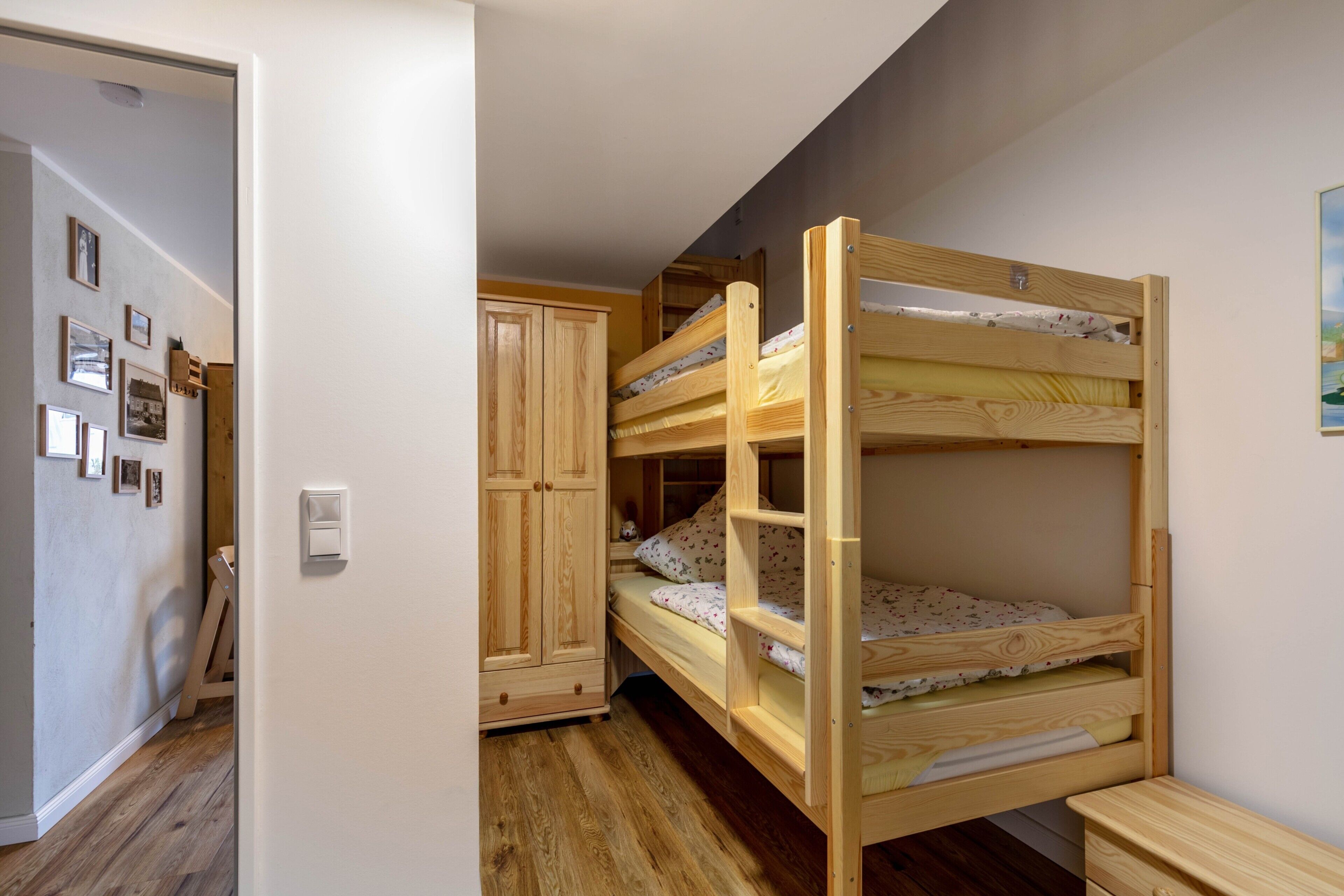 Une chambre avec des lits superposés, une armoire en bois et une porte donnant sur une autre pièce.