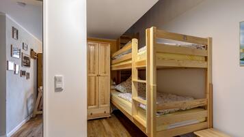 Une chambre avec des lits superposés, une armoire en bois et une porte donnant sur une autre pièce.