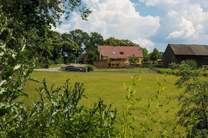 A rural landscape with a large barn, a house with a red roof, and a grassy field.