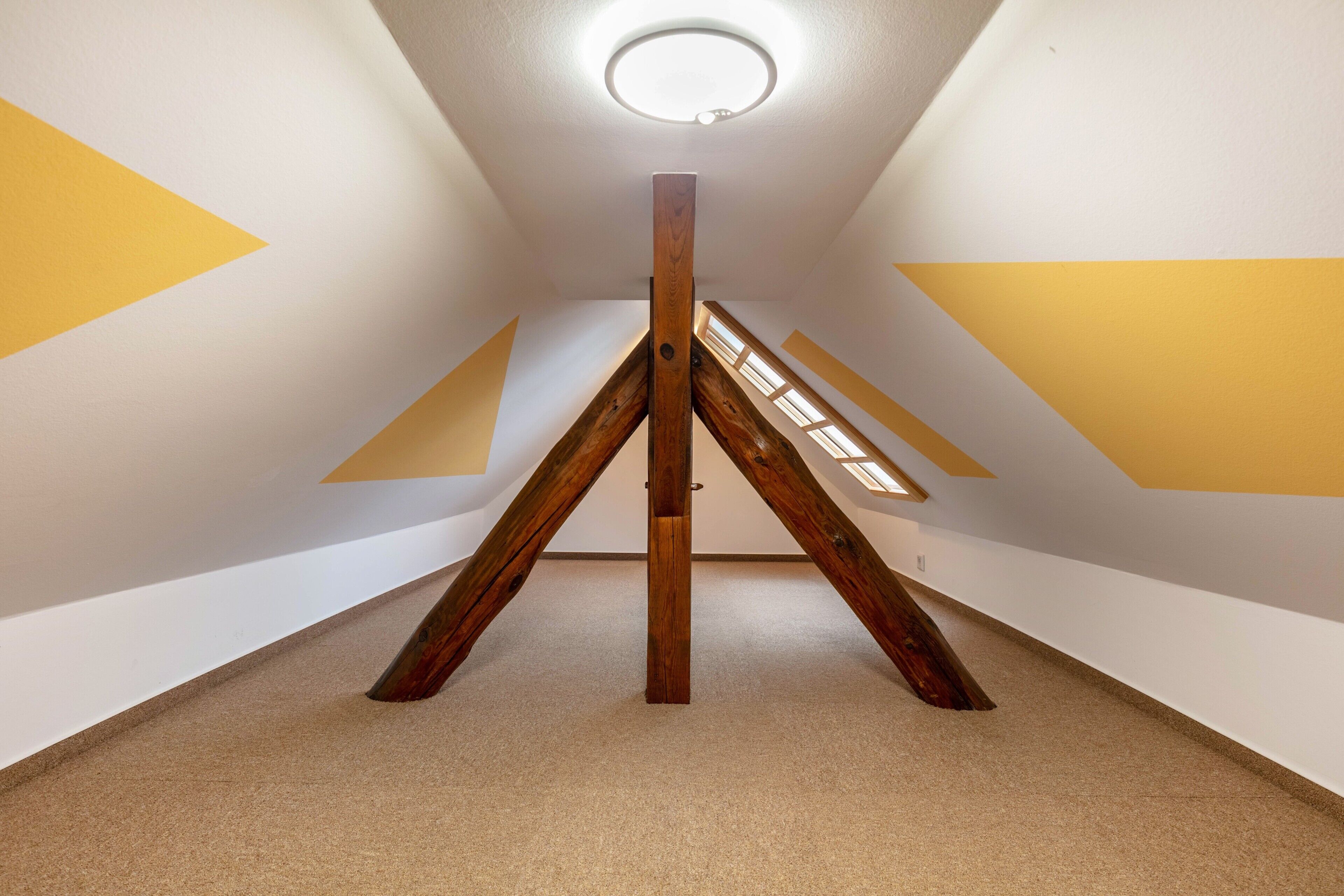 A room with a sloped ceiling, wooden beams, and a central light fixture.