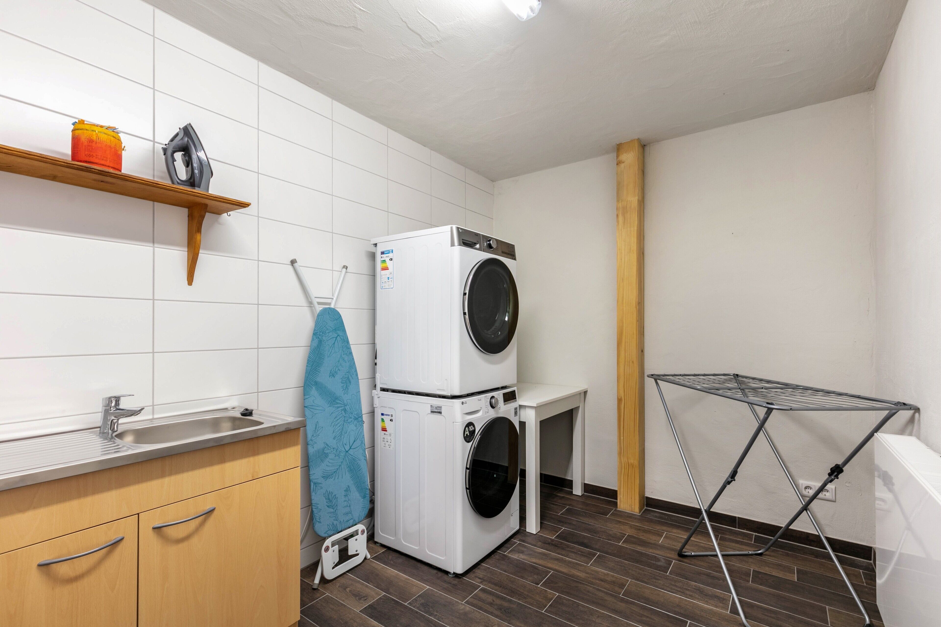 Un espace buanderie comprenant un lave-linge, un étendoir, un évier et des armoires en bois.