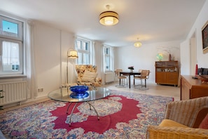 Un salon comprenant une table basse en verre, un canapé à motifs floraux, une table à manger avec des chaises et un meuble en bois.