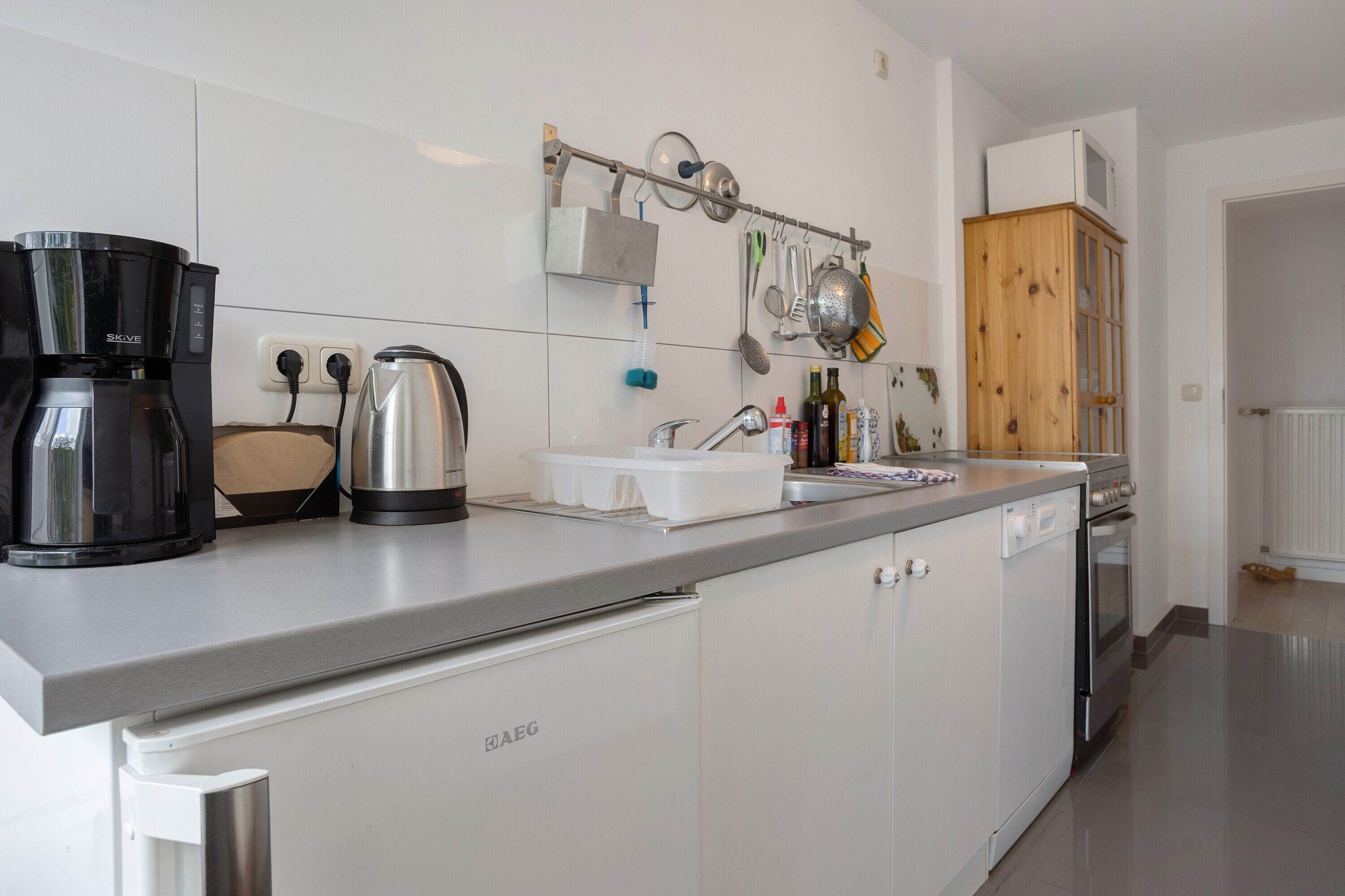 A kitchen with a coffee maker, kettle, and utensils on the counter.
