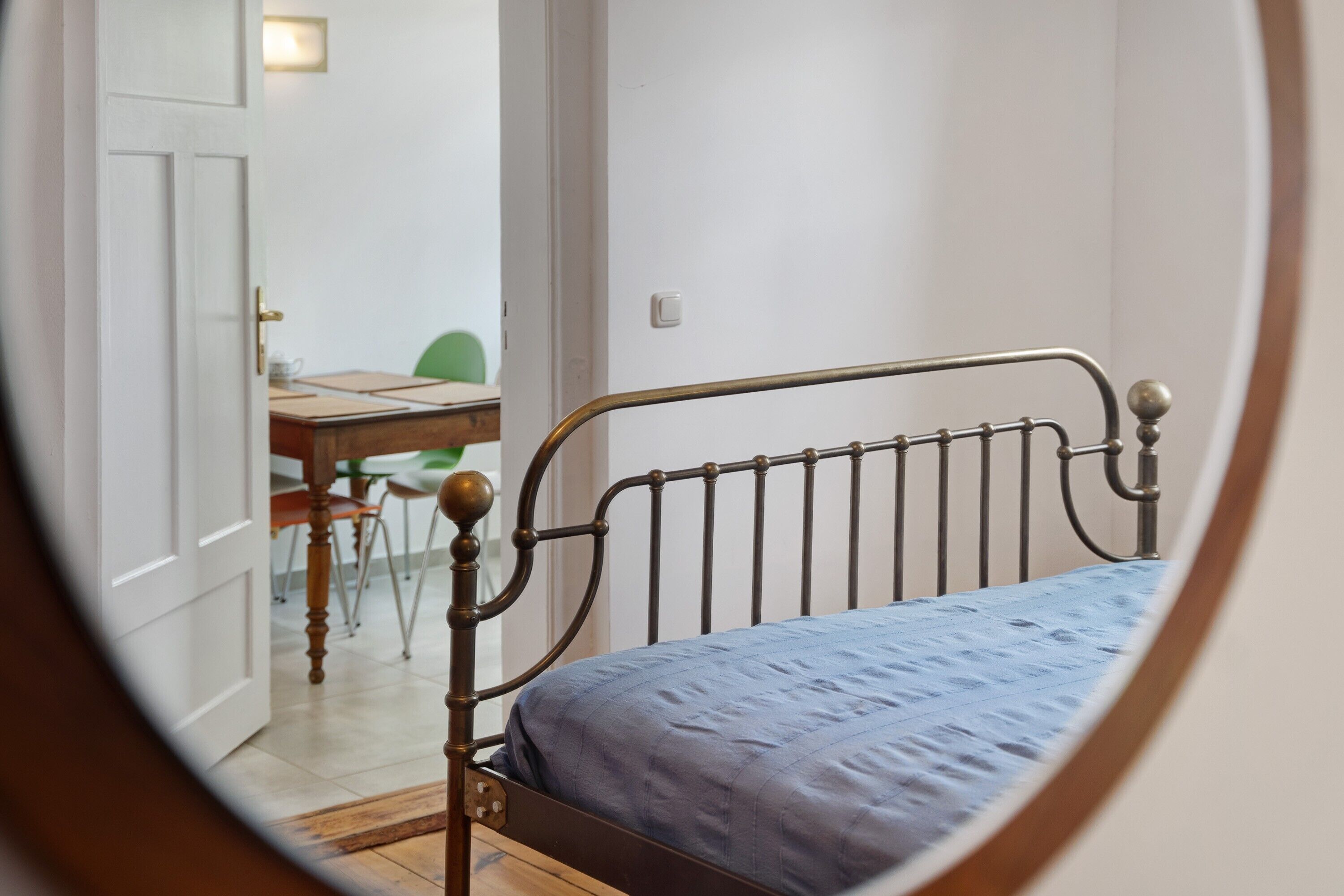 Ein Schlafzimmer mit einem Metallbettgestell, einem Holztisch und einem Stuhl im Hintergrund.