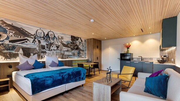 Una habitación de hotel moderna con cama, sofá, mesa de centro y un mural en la pared.