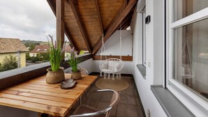 Un balcón con una mesa de madera, dos sillas de mimbre, una silla colgante y plantas en macetas.