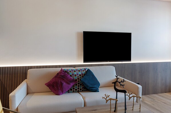 Una sala de estar moderna con un sofá, almohadones decorativos, un televisor montado y una mesa de centro de madera.