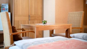 Een kamer met een bed, twee rieten stoelen, een houten tafel en een klein decoratief object op de tafel.