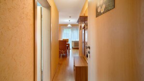 Een gang met een houten bankje, een eethoek met een tafel en stoelen, en een bordje dat aangeeft dat het een appartement is.