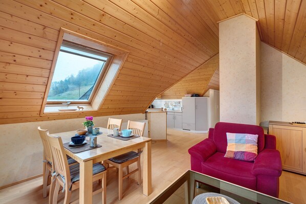 A cozy, wooden interior with a dining area, a red sofa, and a kitchen in the background.