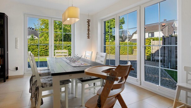 A dining area with a table and chairs, large windows, and a hanging light fixture. - Holiday Home 'Ferienhaus Strandperle' with Private Terrace, Private Garden and Wi-Fi (Ostseebad Zingst)