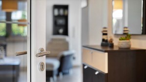 A modern interior with a glass door, a wooden cabinet, and a mirror reflecting a plant. - Holiday Home 'Ferienhaus Strandperle' with Private Terrace, Private Garden and Wi-Fi (Ostseebad Zingst)