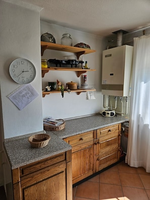 Une cuisine avec des meubles en bois, un plan de travail en granit, une horloge et un chauffe-eau fixé au mur.