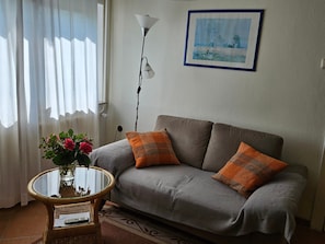 Un salon avec un canapé, une table en verre ornée d’un vase de fleurs, une lampe et un tableau accroché au mur.