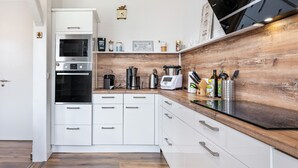 Una cucina moderna con mobili bianchi, una parete decorata in legno, un forno integrato, una macchina da caffè e diversi utensili da cucina.