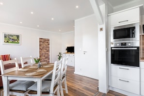 Une cuisine moderne avec des meubles blancs, un four encastré et un coin repas comprenant une table et des chaises en bois.