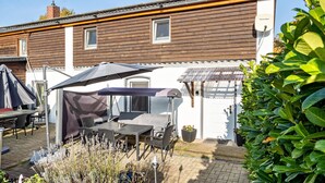 A patio with a table and chairs, a covered umbrella, and a white building with a brown roof. - Pet-Friendly Apartment in the Lake District (Fünfseen Ot Petersdorf)