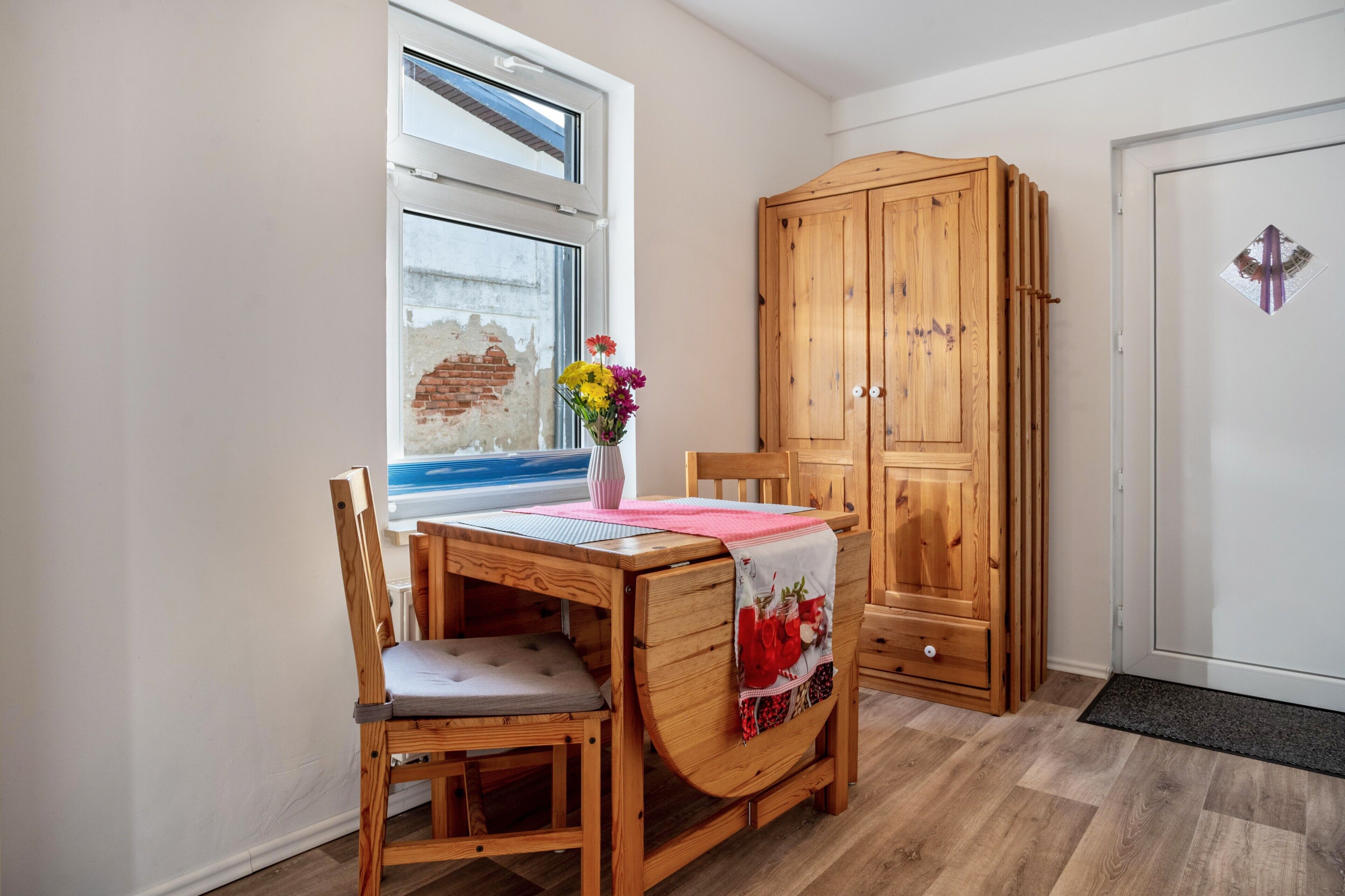 Una mesa de comedor de madera con una silla, un mueble de madera y una ventana que da a un muro de ladrillo.