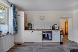 A modern kitchen with white cabinetry, a built-in oven, a coffee maker, and a clock on the wall.