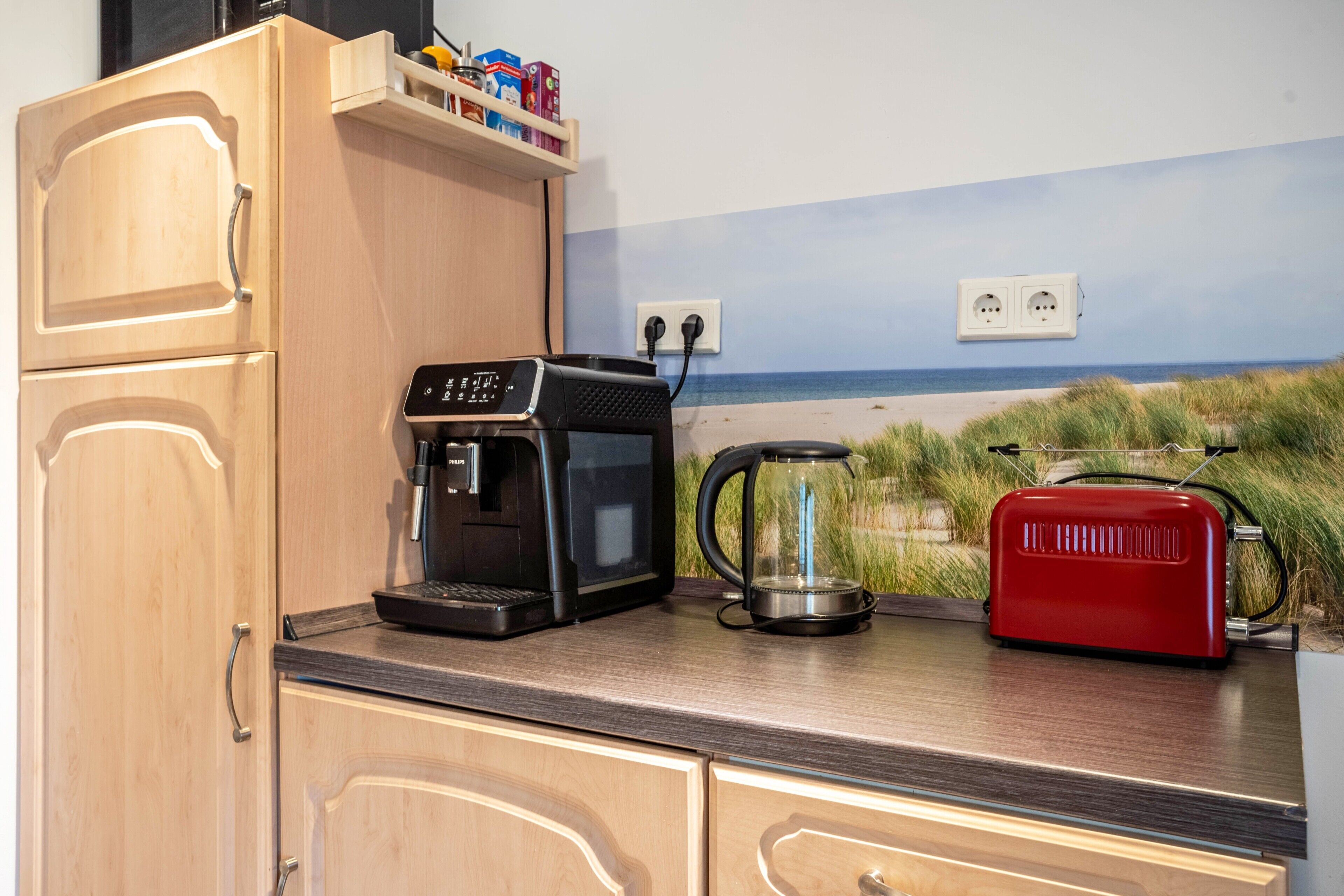 A kitchen with a coffee maker, a red toaster, and a wall outlet.