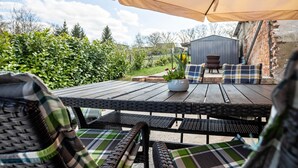 Un patio al aire libre con mobiliario de mimbre, una mesa con un florero y un muro de ladrillo al fondo.