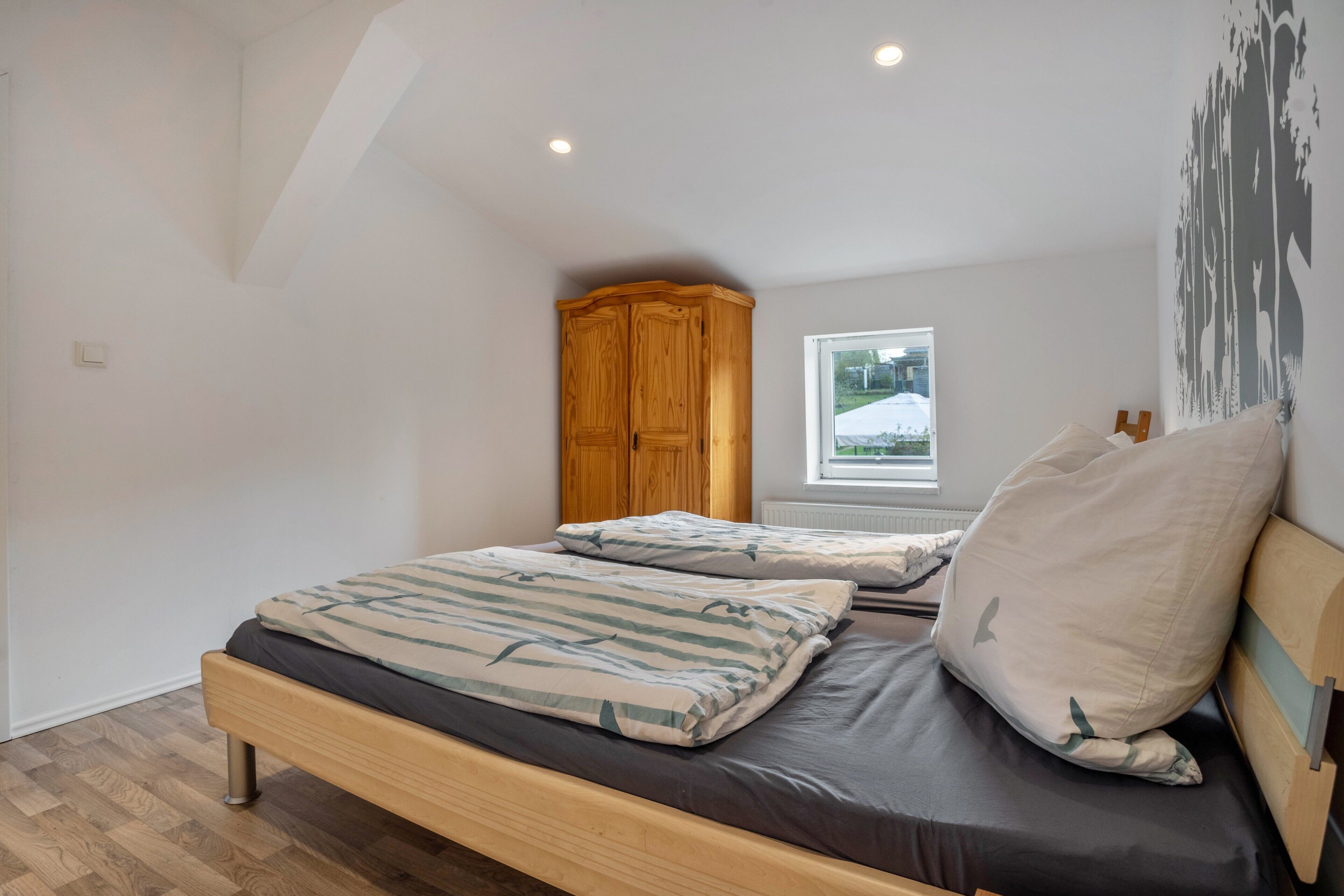 Een slaapkamer met een houten bed, een raam met uitzicht op een besneeerd landschap en een houten garderobe.