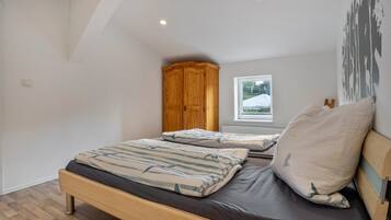 Een slaapkamer met een houten bed, een raam met uitzicht op een besneeerd landschap en een houten garderobe.