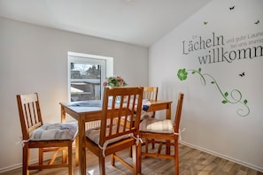 A dining area with wooden chairs and a table, a window, and a wall with a welcome message.