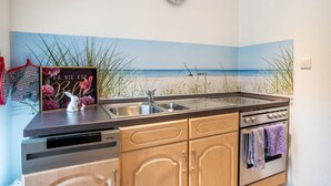 Una cocina con un reloj, un lavamanos, un lavavajillas, armarios de madera y un mural de playa en la pared.