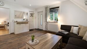 A modern living room with a sofa, a coffee table, and a kitchen area with cabinets and a countertop. - Apartment 'Kleine Nock' with Balcony and Wi-Fi (Burg (Dithmarschen))