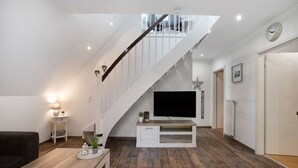 A modern living room with a staircase, a flat-screen TV, and a white entertainment unit. - Apartment 'Kleine Nock' with Balcony and Wi-Fi (Burg (Dithmarschen))