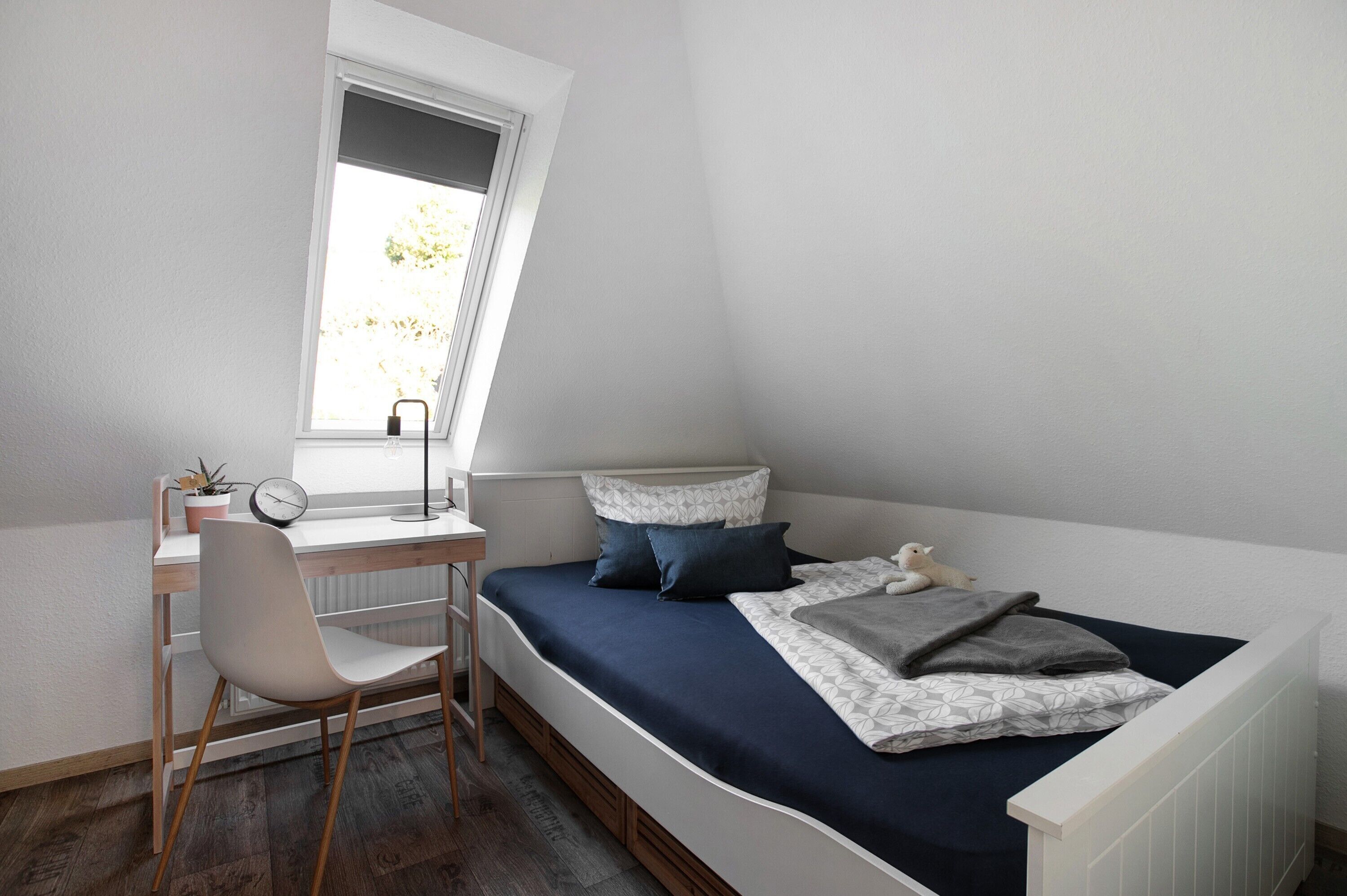 A bedroom with a desk, chair, and a bed with pillows and a blanket.