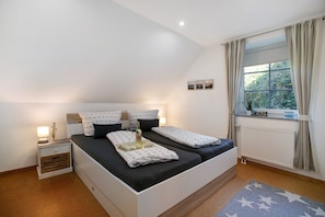 A bedroom with a bed, bedside tables, a window with curtains, and a radiator.