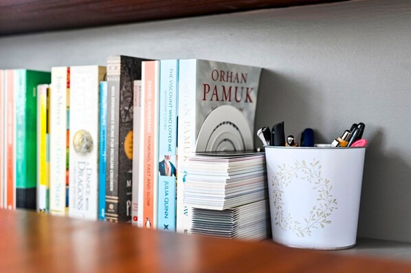 A bookshelf with a variety of books, a stack of notebooks, and a pen holder with pens.