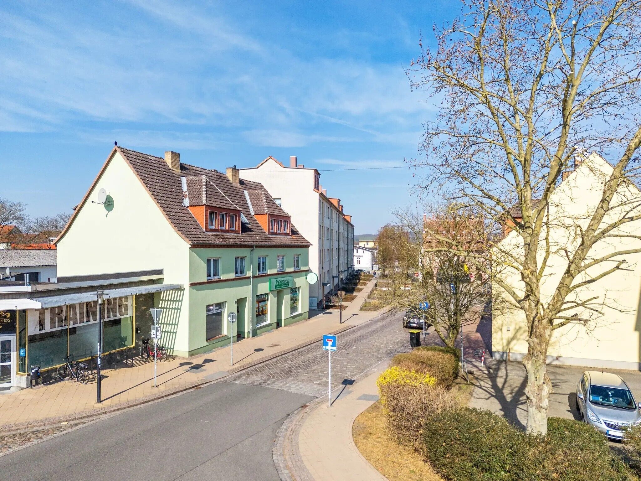 Straßenansicht mit Gebäuden, einer Straße und einem Baum.
