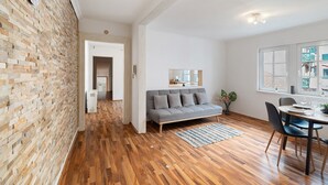 A modern living room with a wooden floor, a grey sofa, a dining table with chairs, and a brick wall. - Apartment 'Albau-wohnung Im Loftstyle' with Wi-Fi (Pforzheim)