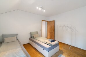 A compact bedroom with a bed, a small seating area, a wooden wardrobe, and a clothing rack. - Apartment 'Albau-wohnung Im Loftstyle' with Wi-Fi (Pforzheim)