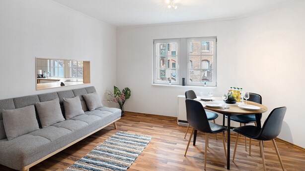 A modern living room with a sofa, dining table, chairs, and a view of buildings through the window. - Apartment 'Albau-wohnung Im Loftstyle' with Wi-Fi (Pforzheim)