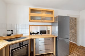 A modern kitchen with a built-in oven, a stainless steel refrigerator, wooden cabinets, and a glass-top island. - Apartment 'Albau-wohnung Im Loftstyle' with Wi-Fi (Pforzheim)