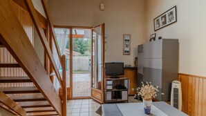 Une pièce avec un escalier en bois, un téléviseur posé sur un meuble en bois, une table avec un vase et un buffet gris.
