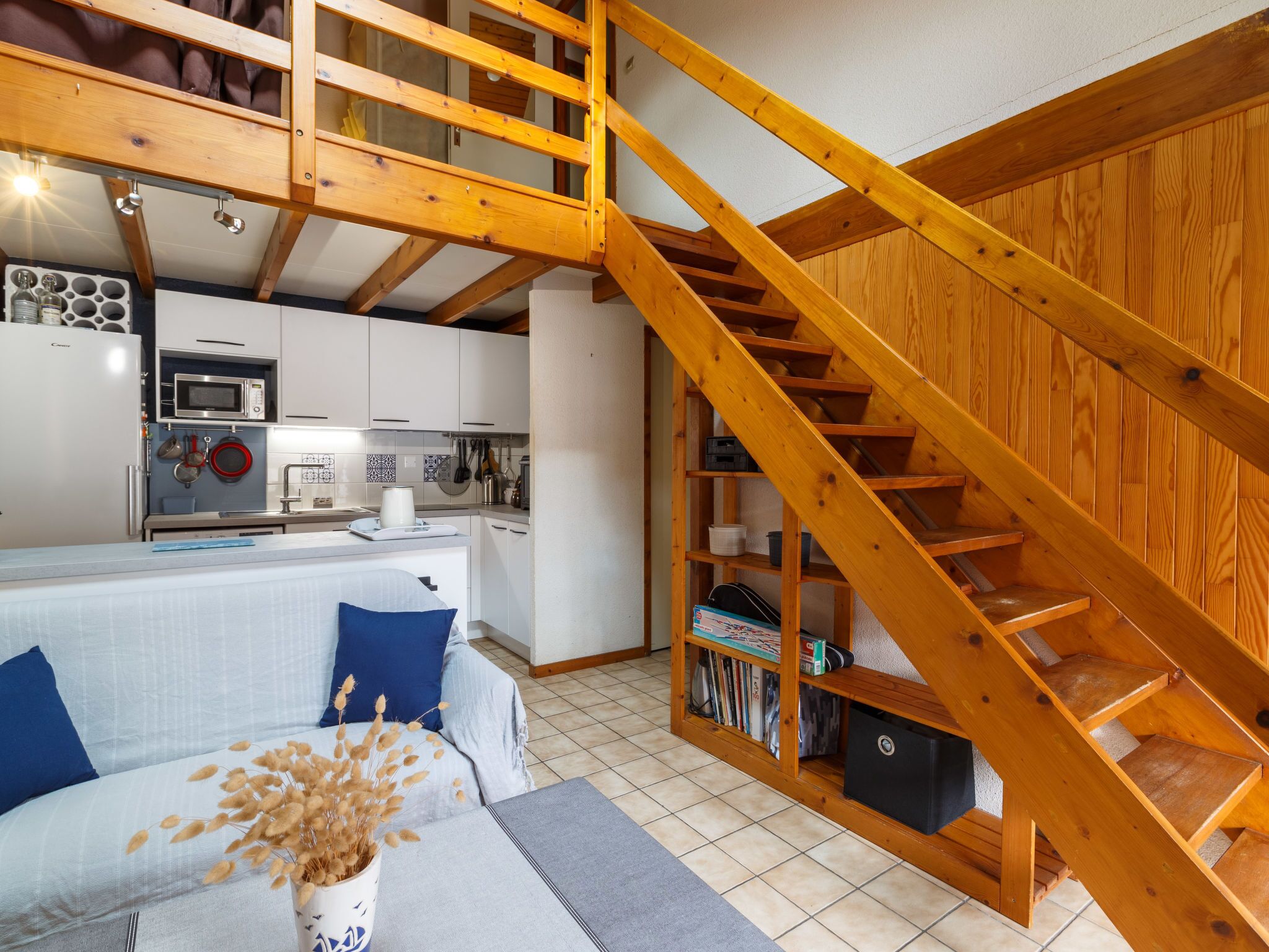Une cuisine moderne avec des meubles blancs, un four à micro-ondes et un évier. Un escalier en bois mène à un niveau supérieur.